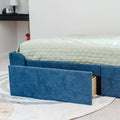 Blue upholstered twin bed frame with open under-bed storage drawer and mint green quilted mattress cover on a patterned rug in a modern bedroom