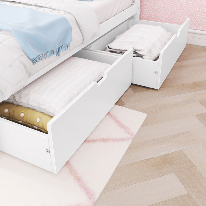 White bed with underbed storage drawers filled with quilts and pillows, blue throw blanket, pink patterned wallpaper and light wood herringbone floor