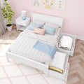 Pastel pink kids bedroom with white twin bed and pull-out trundle storage, soft quilted bedding, blue and blush throw pillows, white nightstand with lamp and potted plant, scallop-pattern pink wallpaper and rainbow wall art