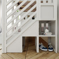 White wooden loft bed staircase with diagonal slat railing and built-in under-stair cubby holding stacked magazines, geometric decor, and navy sneakers on herringbone hardwood floor