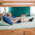 Boy lounging on lower bunk bed petting a fluffy white-and-gray cat on green-and-white striped bedding in a teal kids’ bedroom with a wooden bunk frame