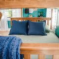 View through bunk bed of colorful kids' bedroom with navy pillows, green-striped bedding, teal accent wall, lightning-bolt curtains, desk lamp and plant
