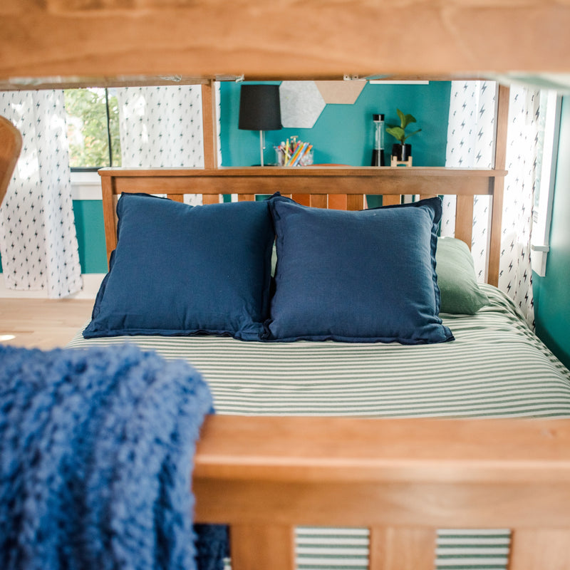 View through bunk bed of colorful kids' bedroom with navy pillows, green-striped bedding, teal accent wall, lightning-bolt curtains, desk lamp and plant