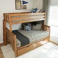 Wooden twin-over-full bunk bed with trundle and built-in storage drawers, gray linen bedding and blue Union Jack accent pillows in a bright kids' bedroom