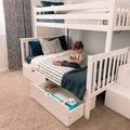 Young child reading on a white bunk bed with pull-out underbed storage drawers and navy striped bedding in a kids' bedroom
