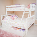 White wooden bunk bed with ladder and under-bed storage drawers, pink and purple bedding and plush pillows in a pastel children's bedroom