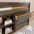 Modern gray wood loft bed with built-in drawers and open shelving, open drawer visible alongside stacked books and a potted plant on hardwood floor rug