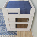 Top-down view of a white wooden twin loft bed with navy blue fitted sheet, blue geometric area rug and hardwood floor in a modern kids' bedroom