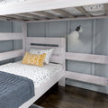 Whitewashed wooden bunk bed in modern kids' bedroom with gray paneled wall, blue quilt, patterned yellow pillow, wall-mounted reading lamp and dark hardwood floor