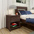 Modern dark wood nightstand in bedroom with gray table lamp, orange alarm clock, stacked children's books and navy blue pillows on bed