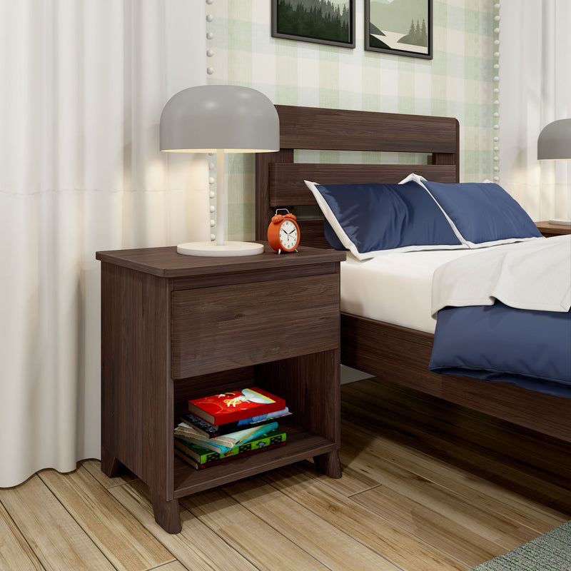 Modern dark wood nightstand in bedroom with gray table lamp, orange alarm clock, stacked children's books and navy blue pillows on bed