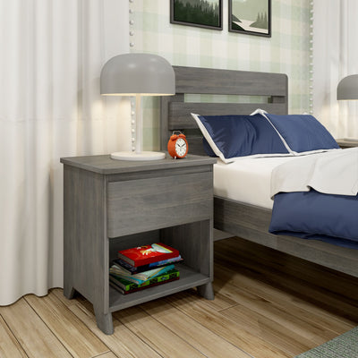 Gray nightstand with white dome lamp and red alarm clock beside gray wood bed with navy pillows and stacked books on hardwood floor in bedroom