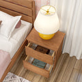 Wooden bedside nightstand with yellow ceramic lamp and two open drawers holding books next to bed on hardwood floor, modern bedroom decor