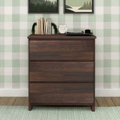 Mid-century modern dark wood dresser with vinyl record player, white alarm clock, stacked books and agate bookends against green plaid wallpaper