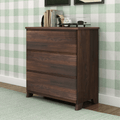 Mid-century modern three-drawer walnut dresser styled with books and alarm clock against green plaid wallpaper — bedroom chest of drawers for storage