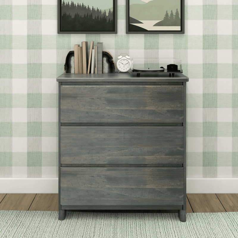 Gray three-drawer wood dresser with turntable, alarm clock and books against green gingham wallpaper in farmhouse-style bedroom