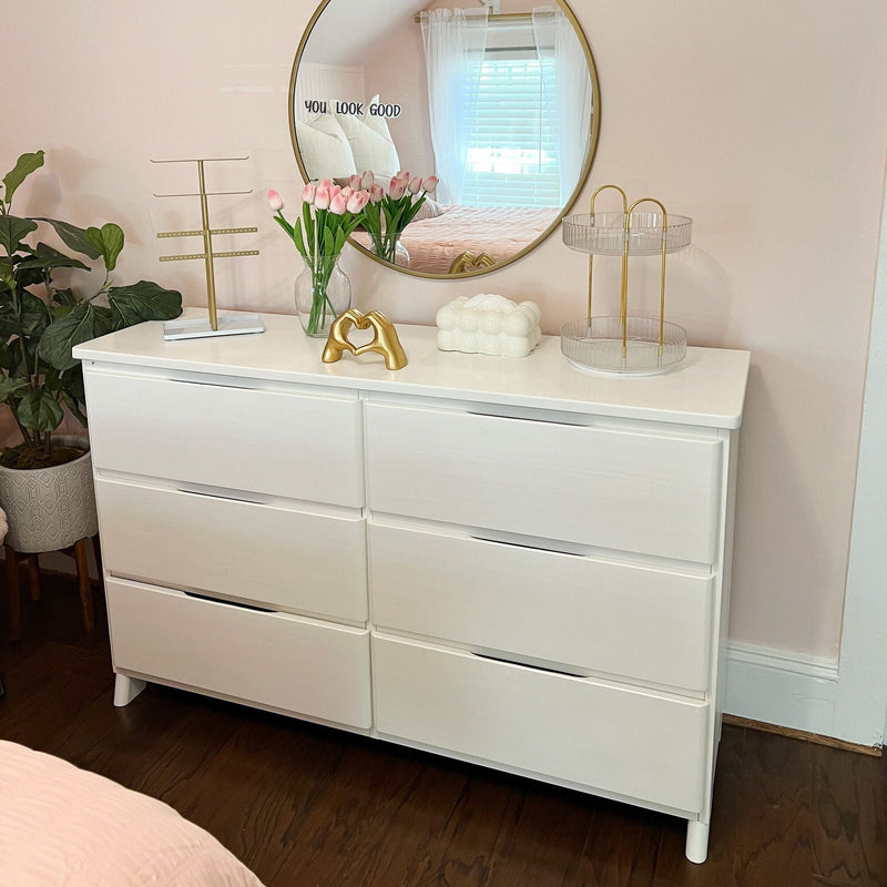 White six-drawer dresser styled with round gold mirror, pink tulips in a glass vase and gold accents in a blush bedroom