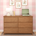 Wooden six-drawer dresser in pink gingham nursery with white table lamp, stacked books, mint green portable record player and framed floral wall art