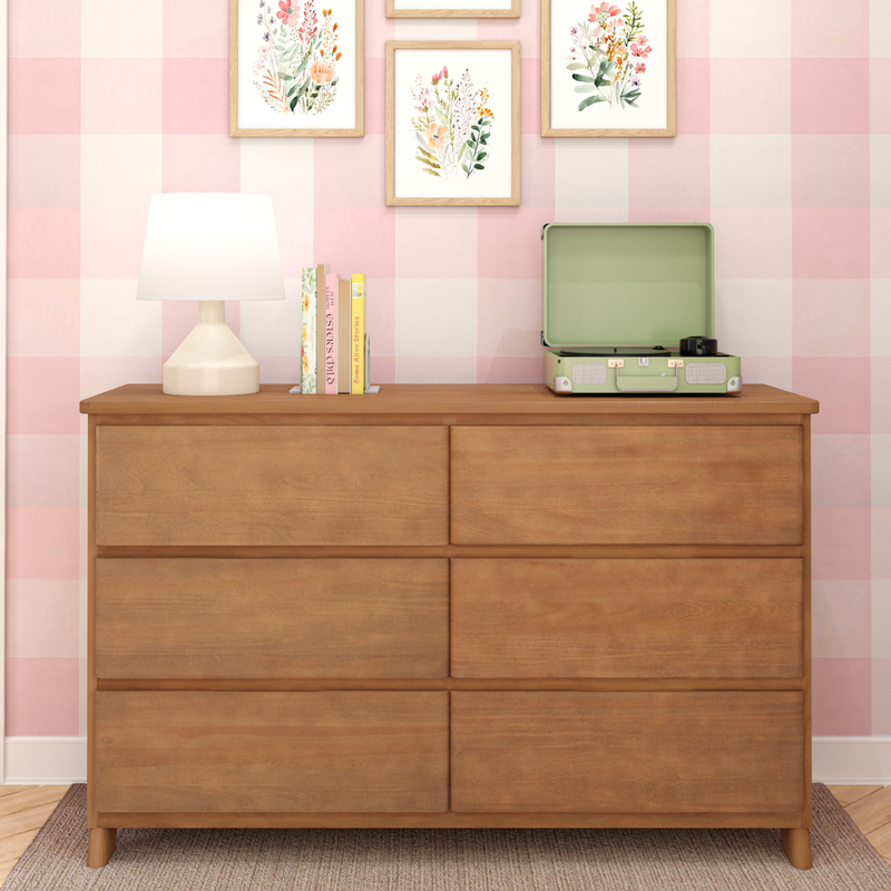 Wooden dresser top with white table lamp, stacked books, mint green record player and framed floral prints on pink gingham wallpaper