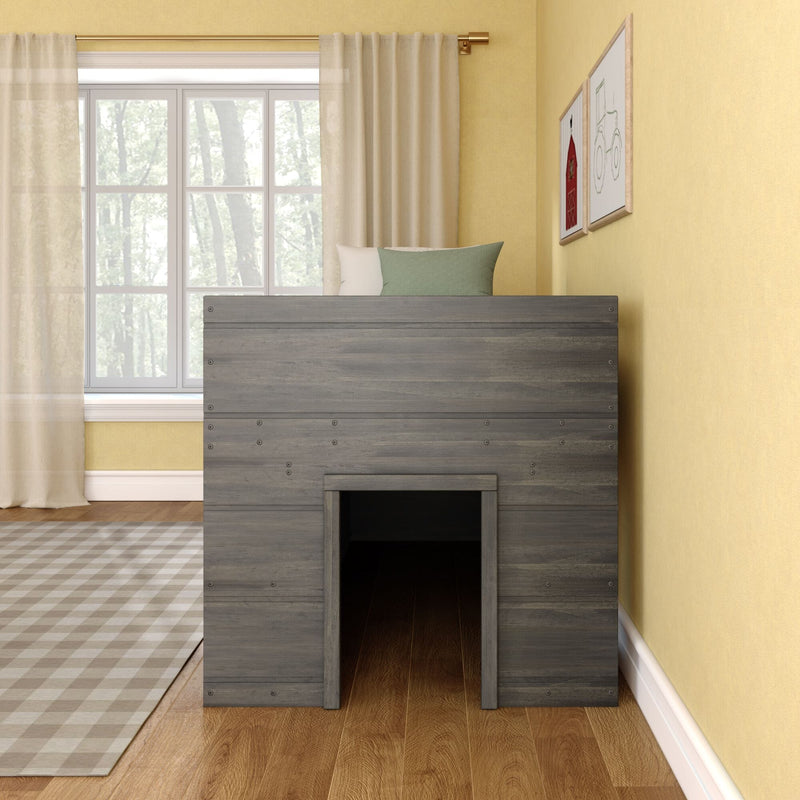 Gray wooden playhouse loft bed with green pillow beside a large sunlit window and sheer curtains in a yellow-walled kids' bedroom with hardwood floors