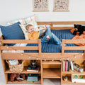 Young boy reading in a cozy kids loft bed with blue quilt, plaid pillows, stuffed bear, string lights and built-in bookshelf storage