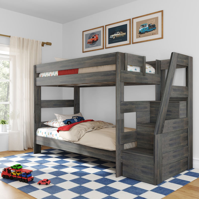 Gray wooden twin-over-twin bunk bed in kids' bedroom with car-themed bedding, toy cars on blue checkered rug, ladder and framed car prints