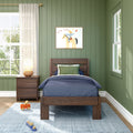 Cozy kids bedroom with green paneled walls, wooden twin bed with navy bedding, framed cowboy art, nightstand lamp, sheer curtains and toys.