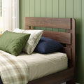 Modern wooden bed headboard with green pillows, plaid duvet and navy cushion against paneled sage green wall and sheer curtain