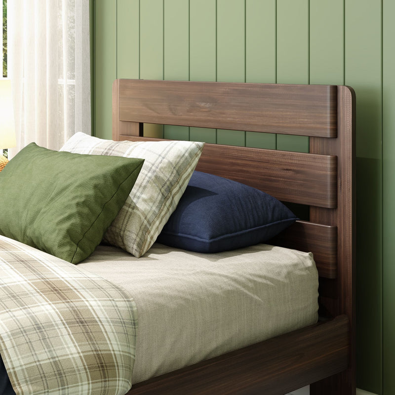 Modern wooden bed headboard with green pillows, plaid duvet and navy cushion against paneled sage green wall and sheer curtain