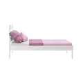 White wooden single bed with pink fitted sheet, two pink pillows and textured pink throw blanket on a modern minimalist frame, isolated on white background