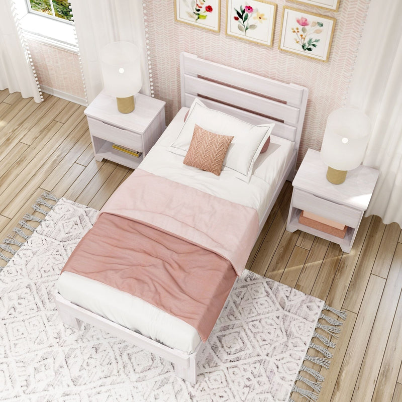 Cozy blush-pink bedroom with white wooden twin bed, matching nightstands and gold-accent table lamps, floral wall art, textured rug on hardwood floor