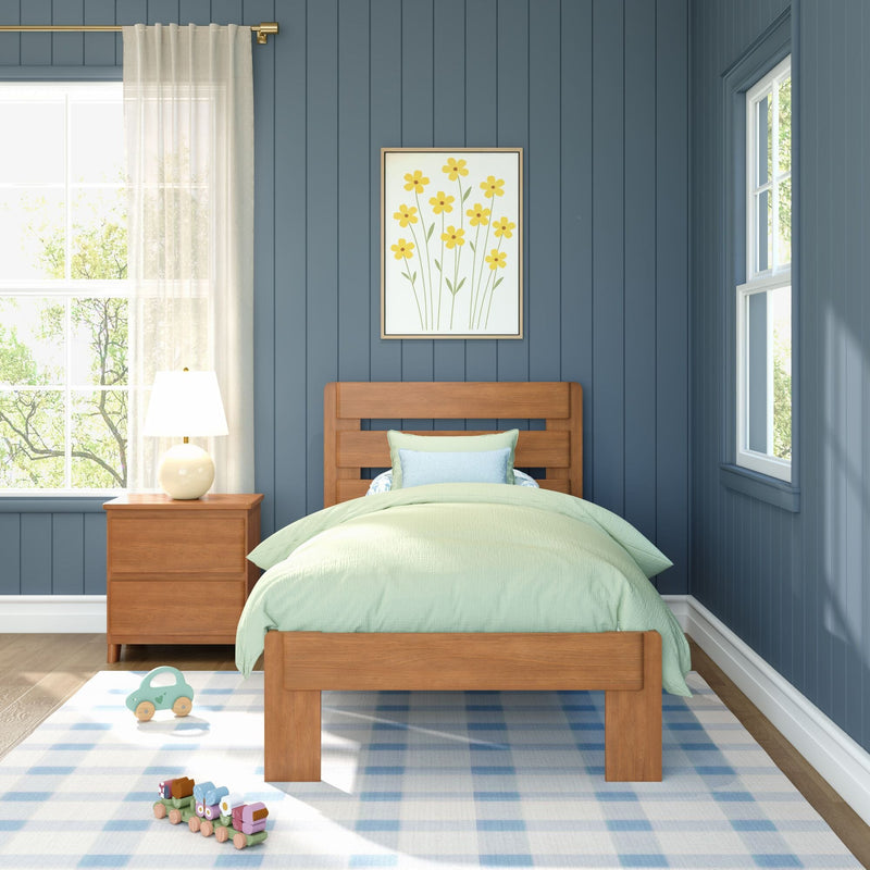 Child's bedroom with wooden single bed and mint-green bedding against a navy blue shiplap wall, framed yellow floral art, wooden nightstand with lamp, plaid rug, and wooden toy train.