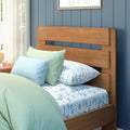 Modern wooden bed headboard against blue paneled wall with mint green and light blue pillows, floral bedding, bedside lamp and sheer curtains