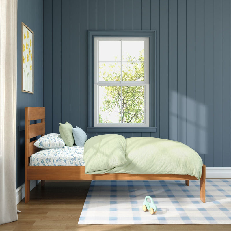 Kids bedroom with blue vertical paneled walls, wooden single bed with green bedding and floral sheets, white-framed window letting in natural light, plaid rug and wooden toy.