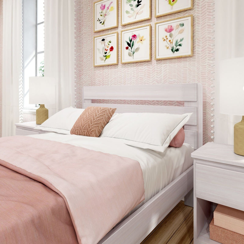 Blush pink bedroom interior with soft pink duvet and throw, textured knit accent pillow, whitewashed wooden platform bed, floral framed wall art and bedside lamp