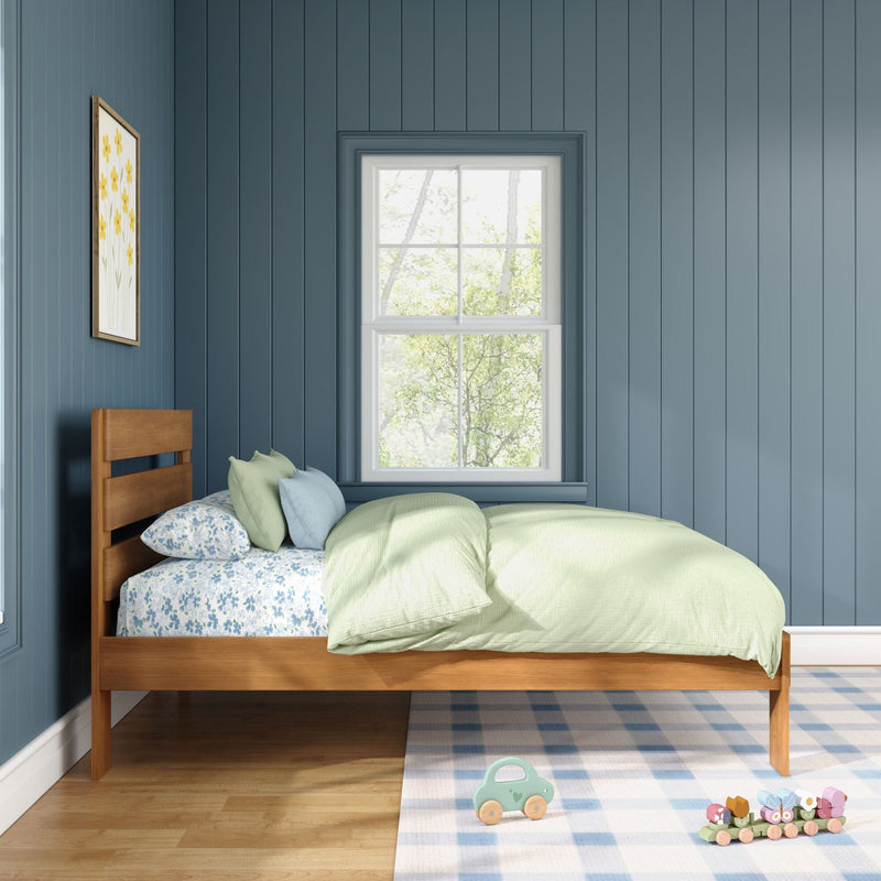 Sunlit children's bedroom with blue vertical paneled walls, wooden twin bed with green duvet and floral sheets, window, plaid rug and wooden toys