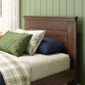 Walnut wood headboard with green pillows, plaid blanket and navy pillow against sage-green paneled wall with sheer curtains in cozy bedroom