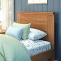 Modern bedroom interior with solid wood bed headboard, mint green quilt, pastel blue pillows and floral blue sheets against a navy shiplap wall and sheer curtains