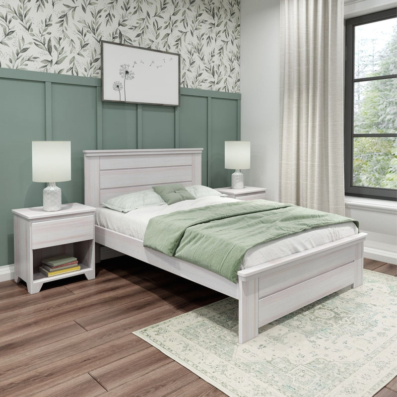 Modern bedroom with sage green board-and-batten accent wall, whitewashed wooden bed and nightstands, light green quilt and pillows, botanical wallpaper, bedside lamps, large window, hardwood floors and patterned area rug