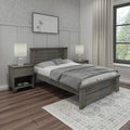 Modern farmhouse bedroom with gray wood bed and matching nightstands, neutral bedding and pillows, glass table lamps, hardwood floors, patterned area rug, botanical wall art and floor-length curtains by a large window
