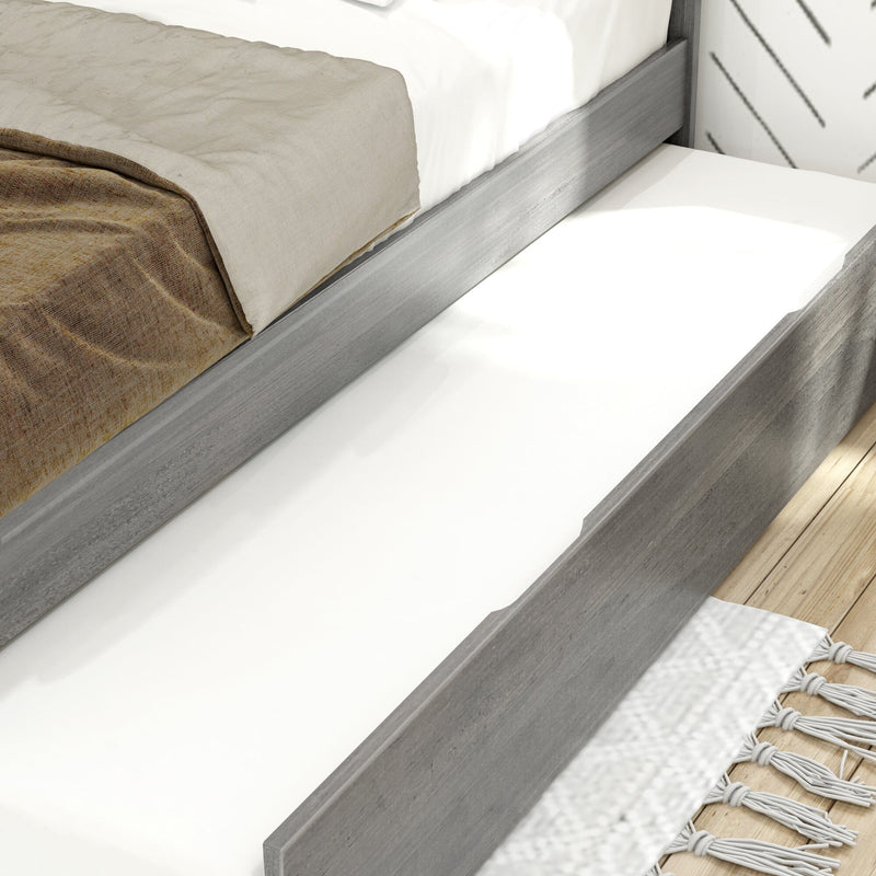 Modern grey wood platform bed with under-bed pull-out trundle drawer, white mattress and beige linen bedding on hardwood floor with white tasseled rug — space-saving bedroom storage solution