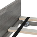 Platform bed frame close-up with grey wood headboard, plywood slats, black center support strap and metal caster wheel