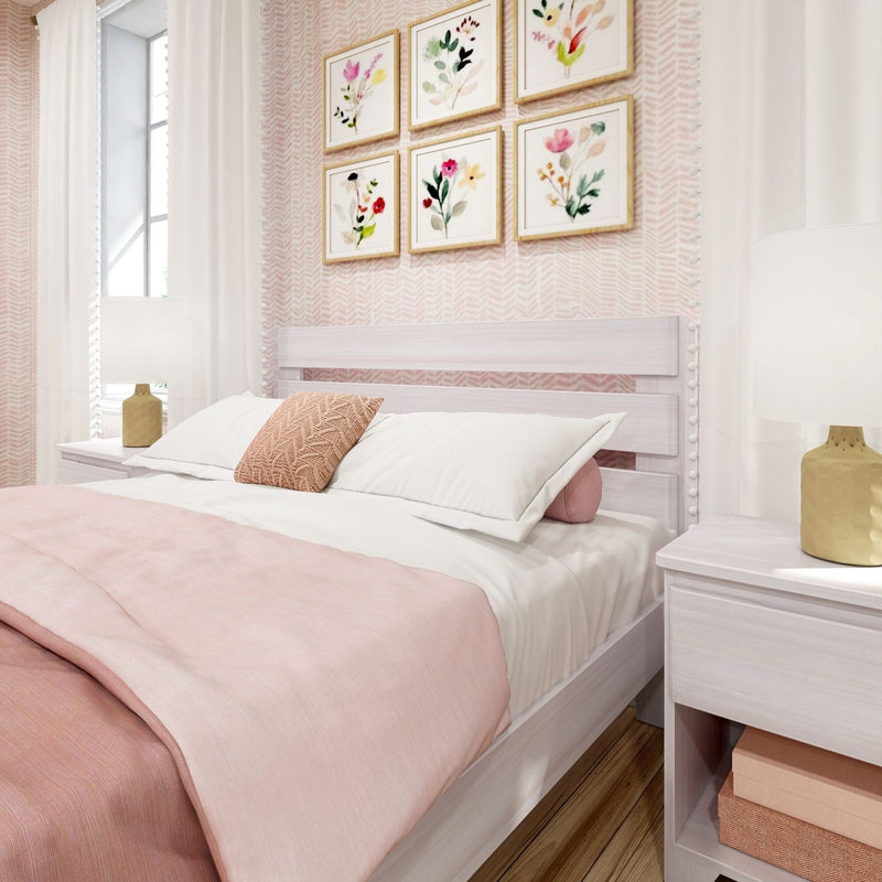 Pastel pink bedroom with white wooden bed, blush bedding and textured throw pillow, bedside ceramic lamp and framed watercolor floral gallery wall