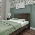 Modern bedroom with sage green bedding, dark wood bed frame, nightstand lamp, teal board-and-batten and botanical wallpaper