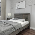 Modern farmhouse bedroom with dark wooden platform bed, gray bedding, paneled accent wall, minimalist dandelion wall art, neutral curtains and bedside lamp