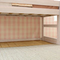 Light wood loft bed frame with ladder and slatted support, pink gingham wallpaper, hardwood floor and woven rug in a child's bedroom