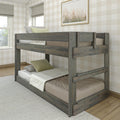 Rustic gray wooden twin-over-twin bunk bed in a neutral farmhouse bedroom with buffalo-check wallpaper, linen bedding, green accent pillows, framed coastal grass art and natural light from windows
