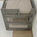 Top view of gray-washed rustic wooden bunk bed frame with beige textured bedding, hardwood floor and light woven area rug
