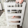 Modern white wooden twin loft bed with ladder, striped black-and-white bedding, pink accent pillows and floor pouf in children's bedroom