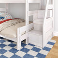 Space-saving whitewashed wooden kids bunk bed with built-in storage stairs, lower bed with car-print pillow, beige bedding and blue check rug